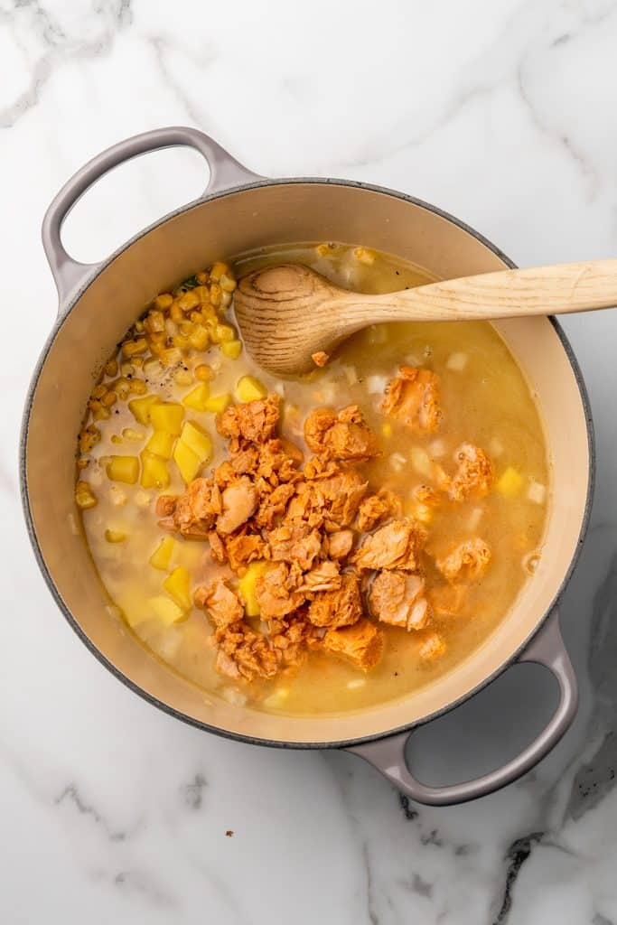 salmon chowder ingredients and a wooden spoon in a gray dutch oven