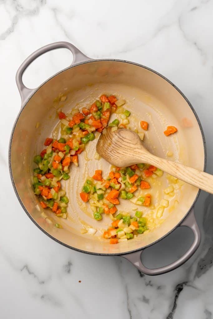flour coated tender vegetables in a dutch oven with a wooden spoon resting on the edge