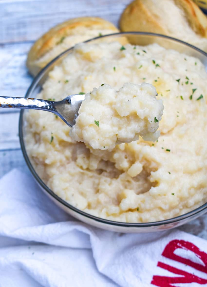 a fork holding up a scoop of mashed potatoes made using canned potatoes above a glass bowl
