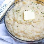 canned mashed potatoes topped with a pat of butter and green herbs in a glass serving bowl