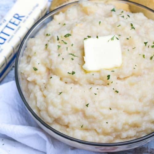 canned mashed potatoes topped with a pat of butter and green herbs in a glass serving bowl