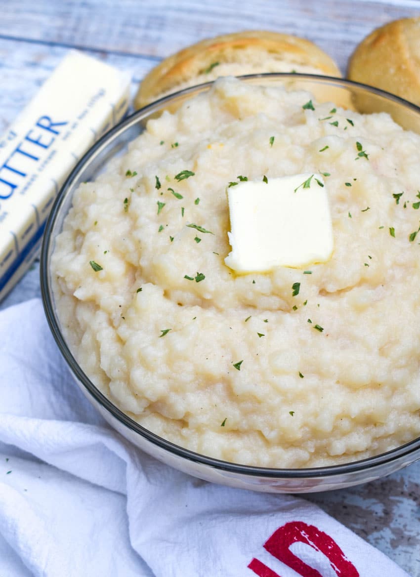 canned mashed potatoes topped with a pat of butter and green herbs in a glass serving bowl