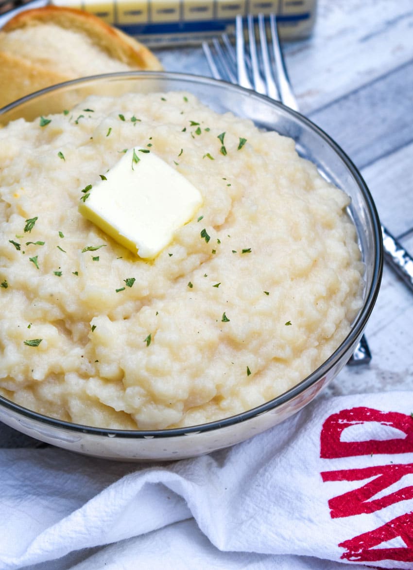 canned mashed potatoes topped with a pat of butter and green herbs in a glass serving bowl
