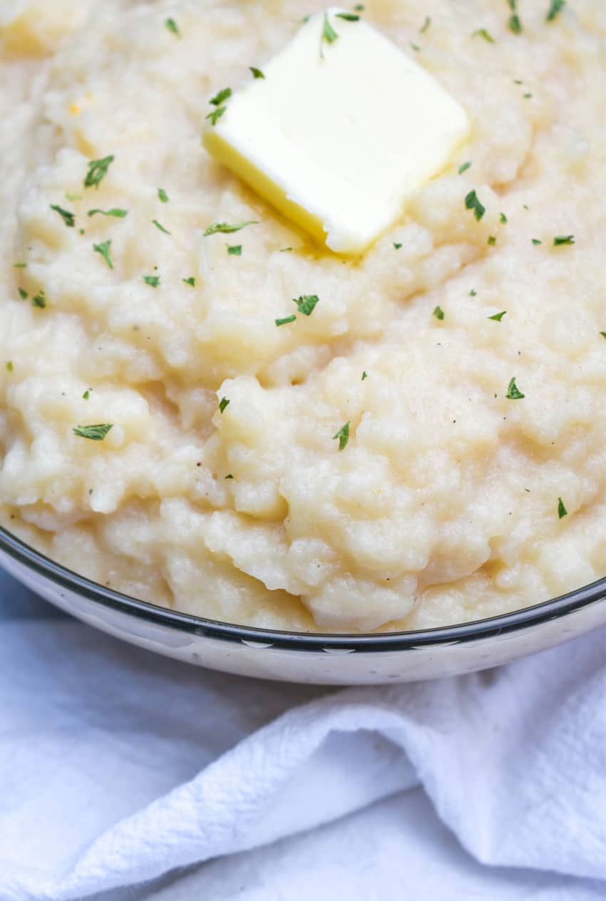 canned mashed potatoes topped with a pat of butter and green herbs in a glass serving bowl
