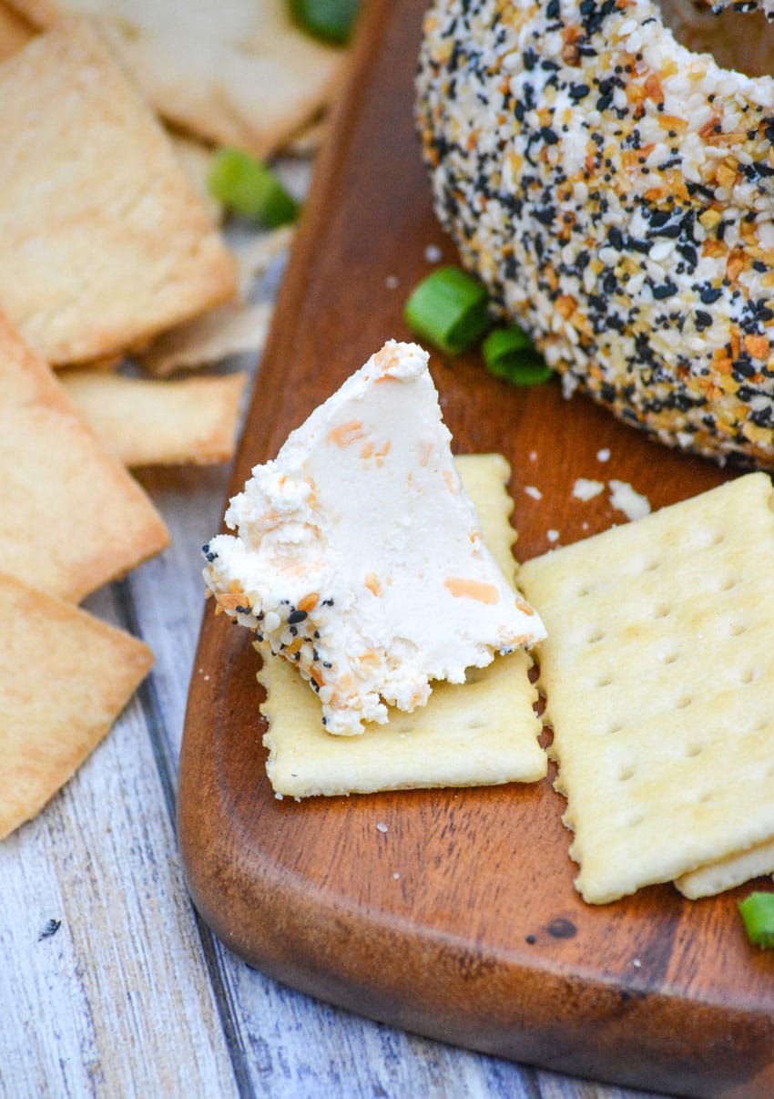 a bit of everything bagel seasoning  coated cheese ball on top of a buttery club cracker laying on a wooden cutting board