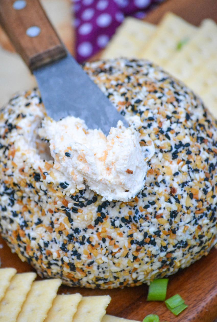 a spreader topped with seasoned cream cheese resting on top of a seed coated cheeseball