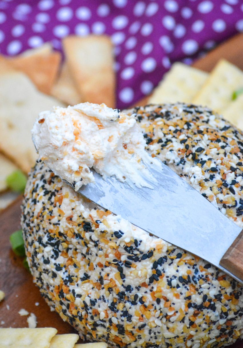 a spreader topped with seasoned cream cheese resting on top of a seed coated cheeseball