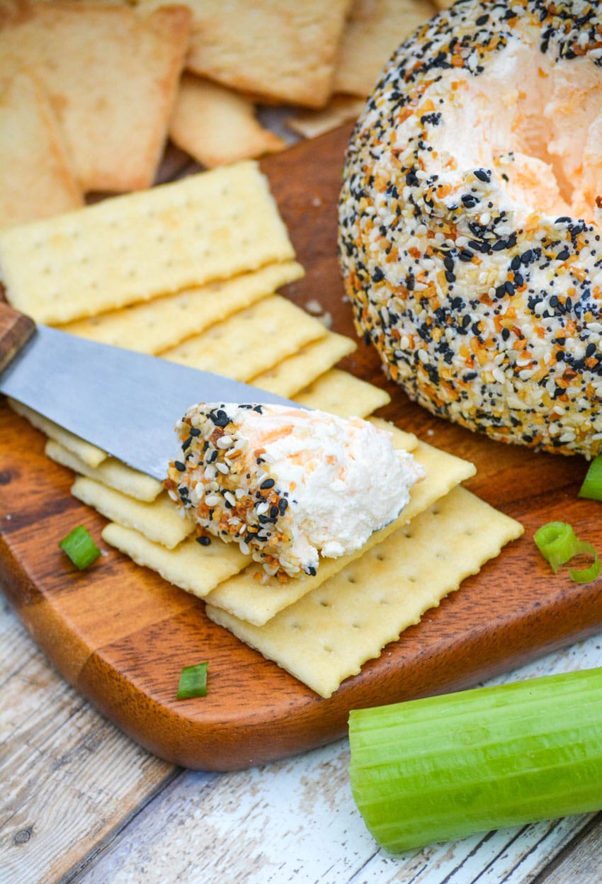 a cheese spread topped with everything bagel seasoning cheese ball resting on buttery crackers