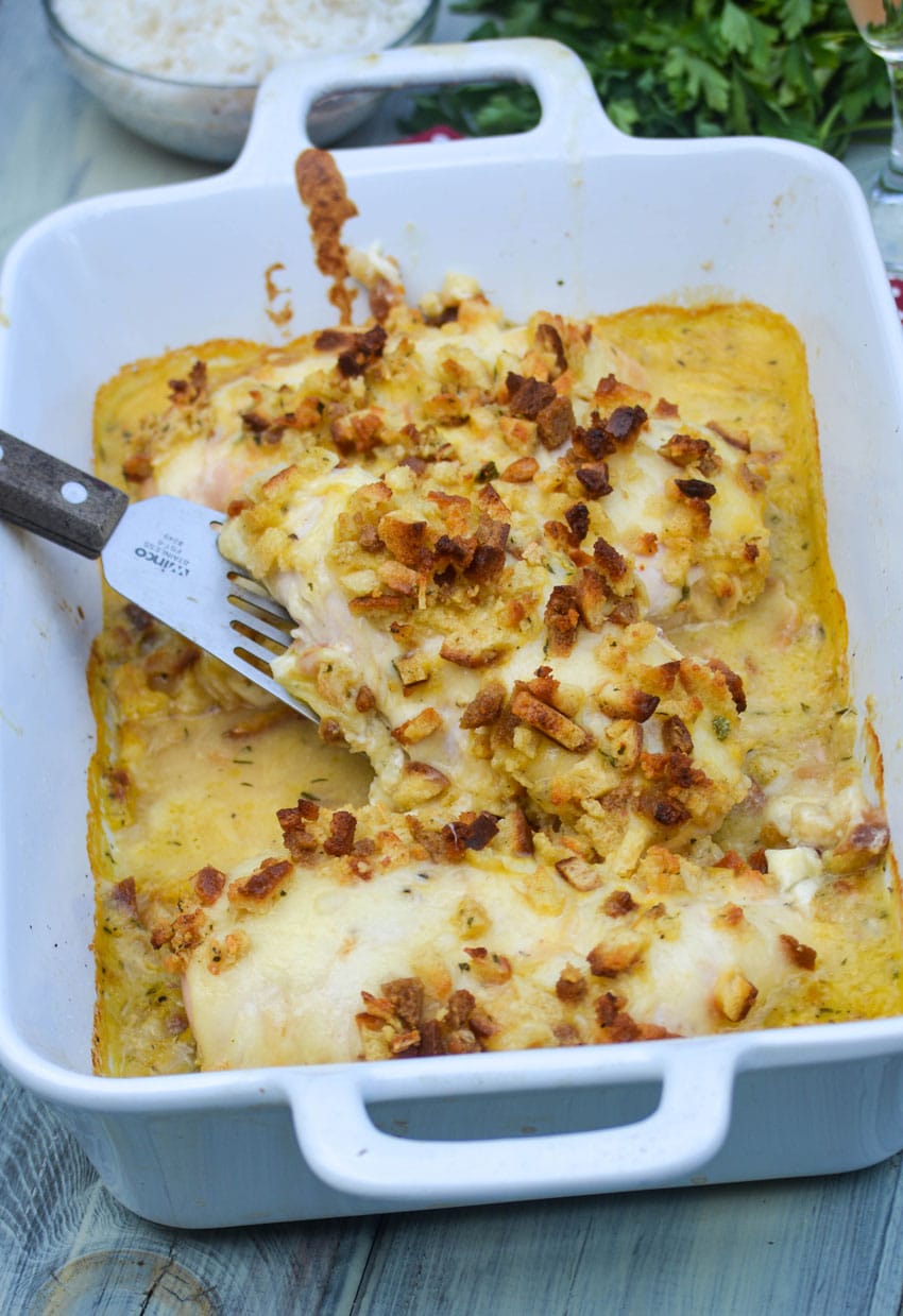 a spatula lifting a piece of herb crusted chicken in wine sauce casserole out of a white baking dish