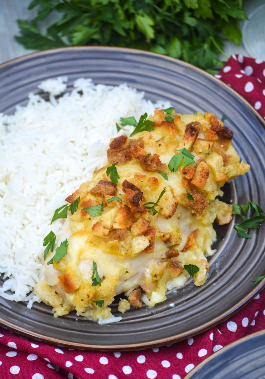 a piece of herb crusted chicken in wine sauce topped with fresh parsley on a brown plate next to steamed white rice