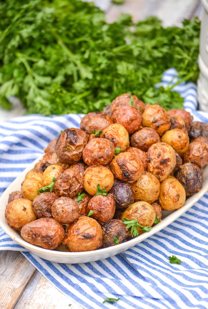 mayonnaise roasted potatoes topped with fresh parsley leaves on an oval serving platter