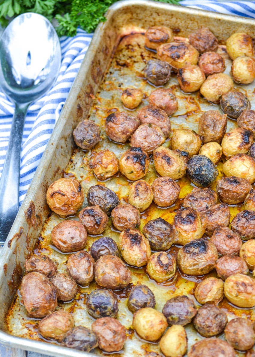mayonnaise roasted potatoes on a rimmed baking sheet with a slotted silver serving spoon on the side