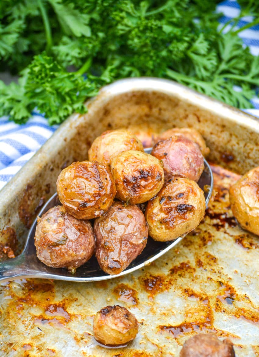 a slotted silver serving spoon full of mayonnaise roasted potatoes resting on a rimmed baking sheet