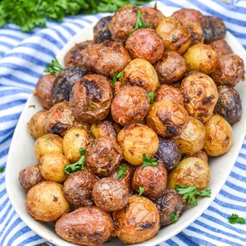 mayonnaise roasted potatoes topped with fresh parsley leaves on an oval serving platter