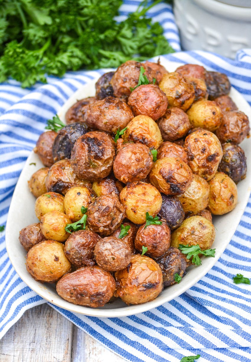 mayonnaise roasted potatoes topped with fresh parsley leaves on an oval serving platter
