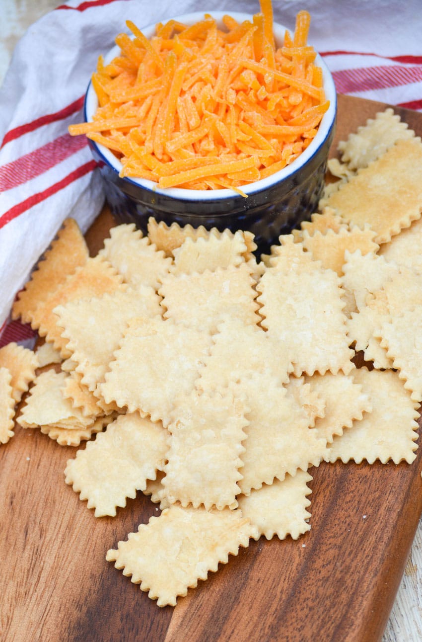 pie crust crackers on a wooden cutting board next to a bowl of shredded cheese