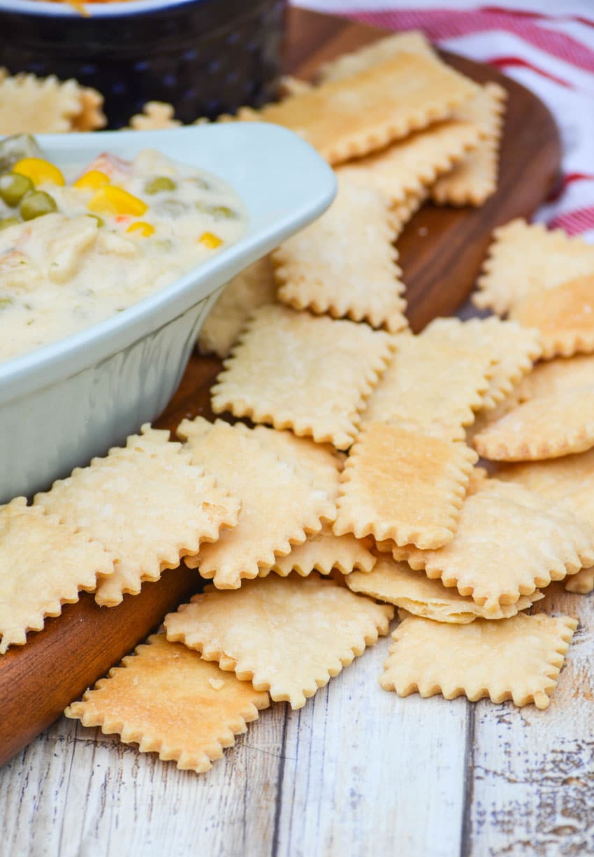 pie crust crackers on a wooden cutting board next to a bowl of chicken soup