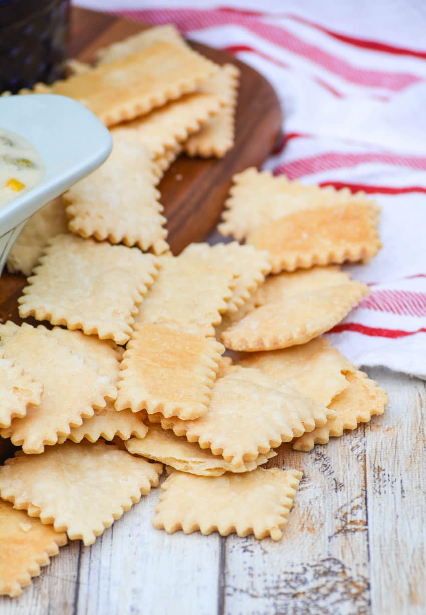 pie crust crackers on a wooden cutting board next to a bowl of chicken soup