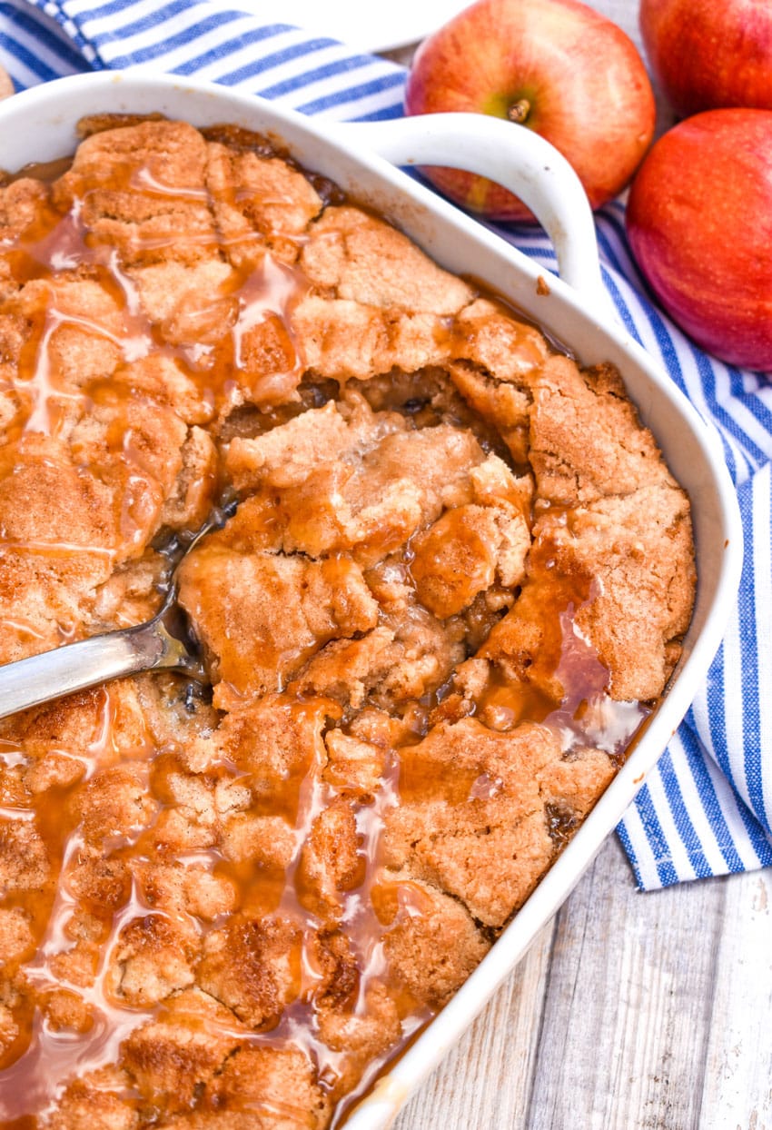 a silver spoon in a white casserole dish filled with snickerdoodle apple cobbler