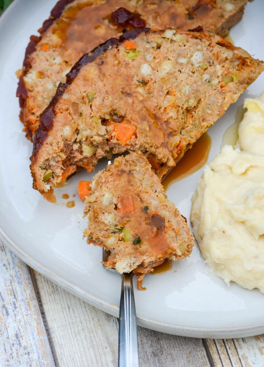 a piece of cranberry turkey meatloaf with gravy on a silver fork resting on a white plate