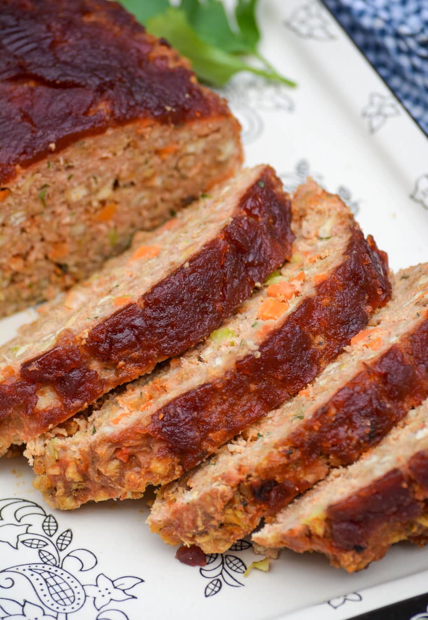slices of cranberry sauce topped turkey meatloaf on a black and white serving platter