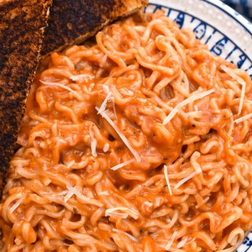 tomato soup ramen in a blue and white bowl with a dark grilled cheese on the side