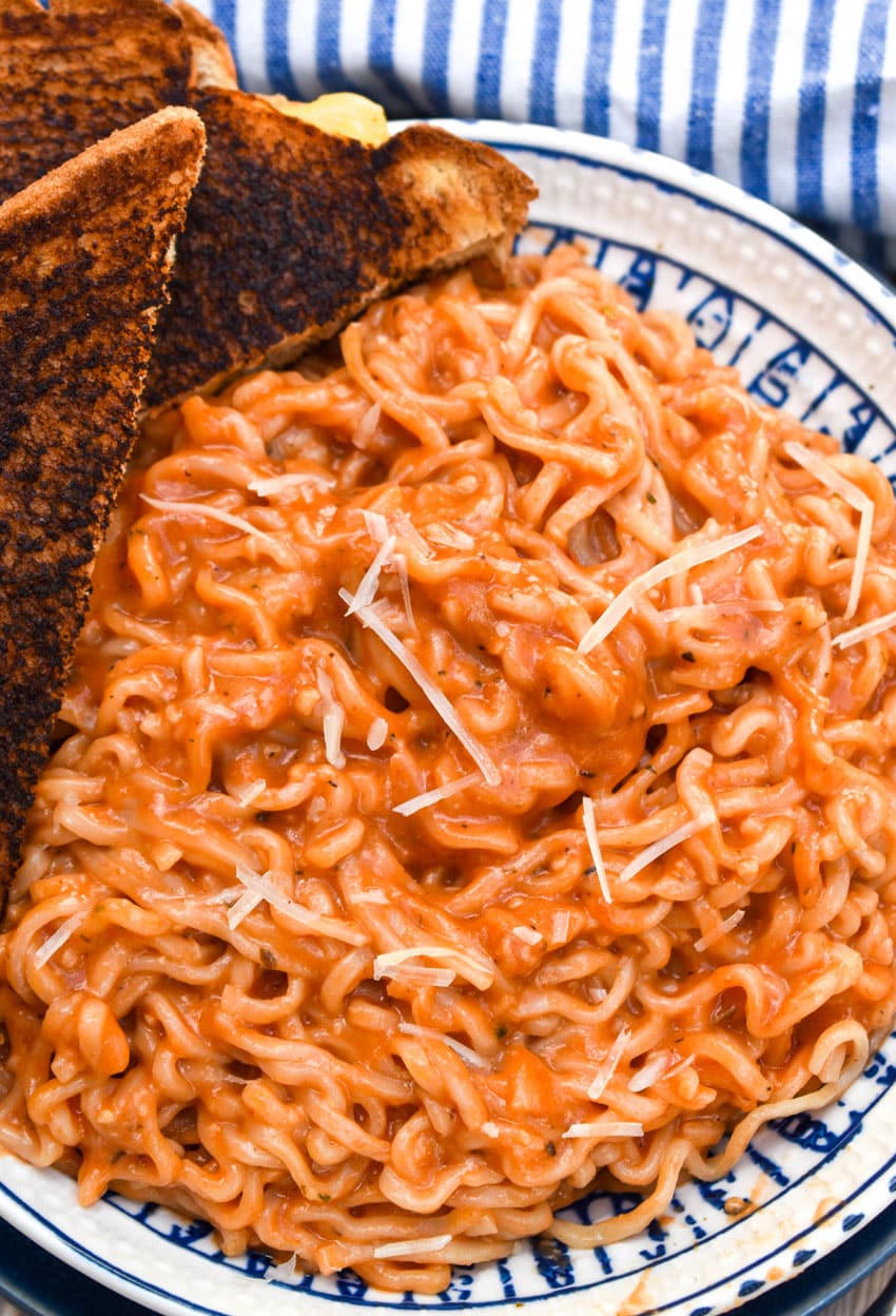 tomato soup ramen in a blue and white bowl with a dark grilled cheese on the side