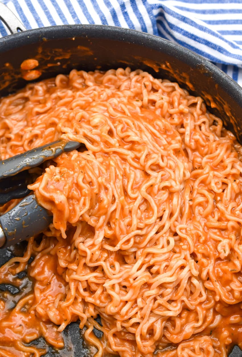 tomato soup ramen in a black skillet with tongs