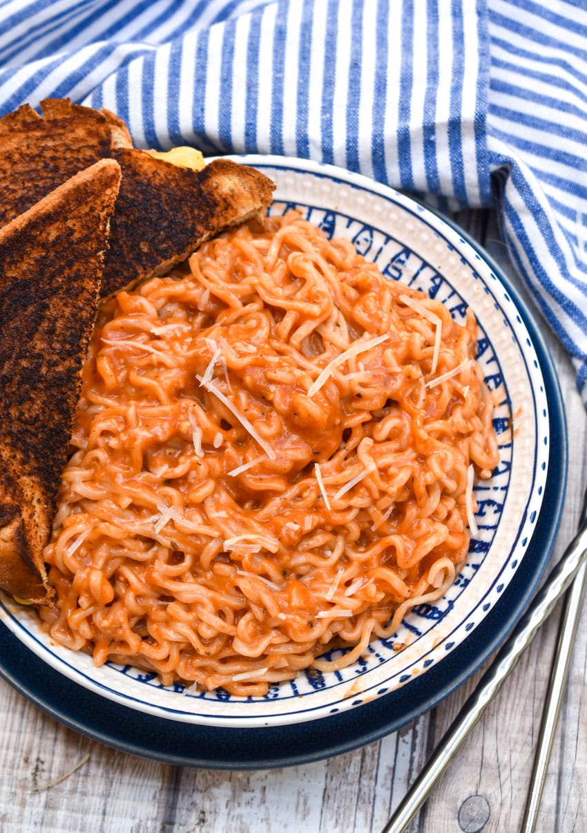 tomato soup ramen in a blue and white bowl with a dark grilled cheese on the side