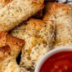 cheesy garlic breadsticks piled next to a small white bowl filled with marinara sauce