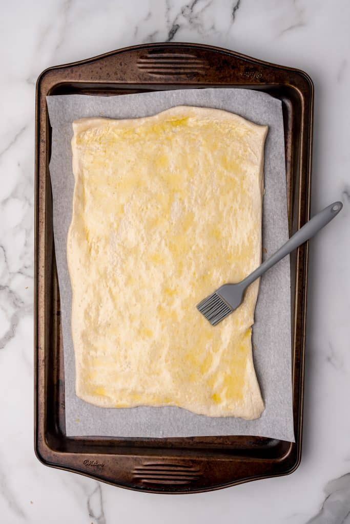 olive oil brushed pizza dough spread on a parchment paper covered baking sheet