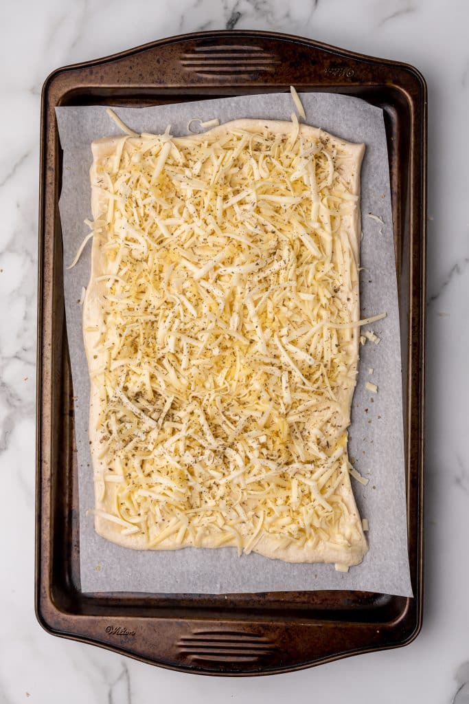 pizza dough covered with shredded cheese on a parchment paper covered baking sheet