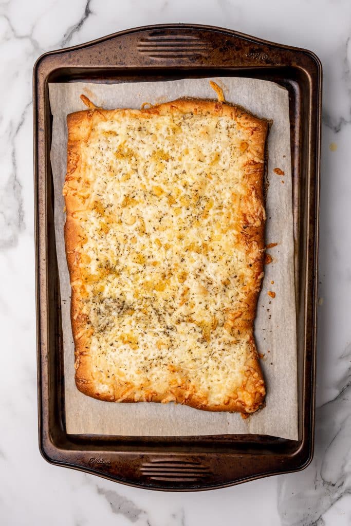 baked rectangular cheesy pizza on a parchment covered baking sheet