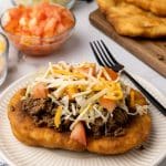 loaded navajo fry bread taco on a white plate next to a black fork