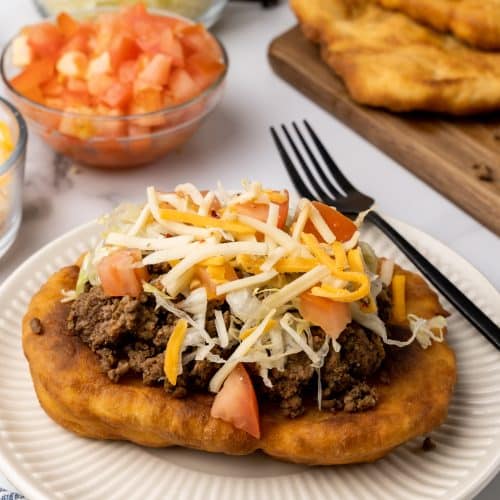 loaded navajo fry bread taco on a white plate next to a black fork