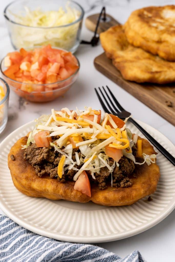 loaded navajo fry bread taco on a white plate next to a black fork