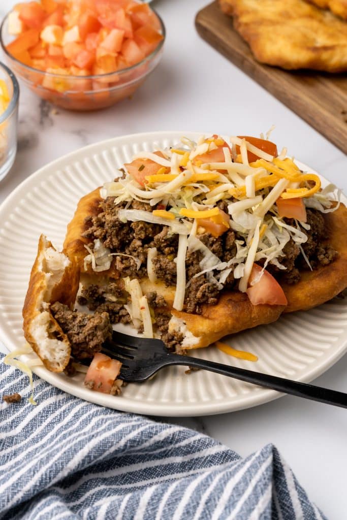 loaded navajo fry bread taco on a white plate next to a black fork
