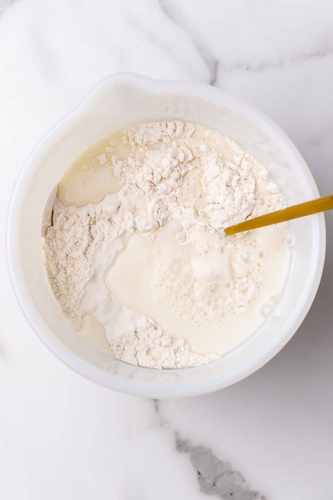 Indian fry bread batter being mixed up in a white bowl with a wooden spoon