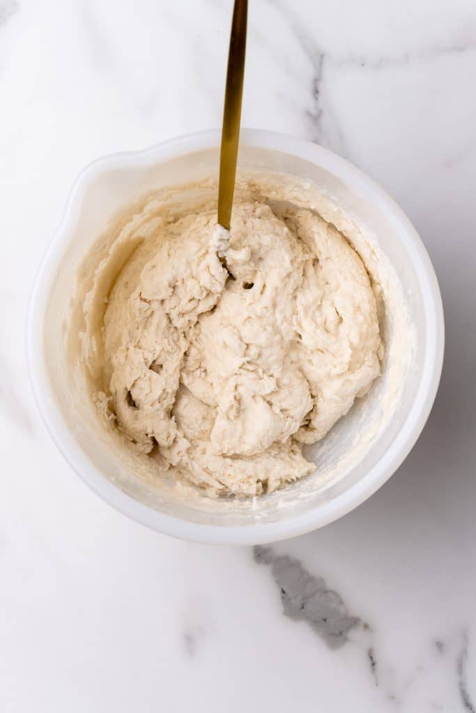 Indian fry bread batter being mixed up in a white bowl with a wooden spoon