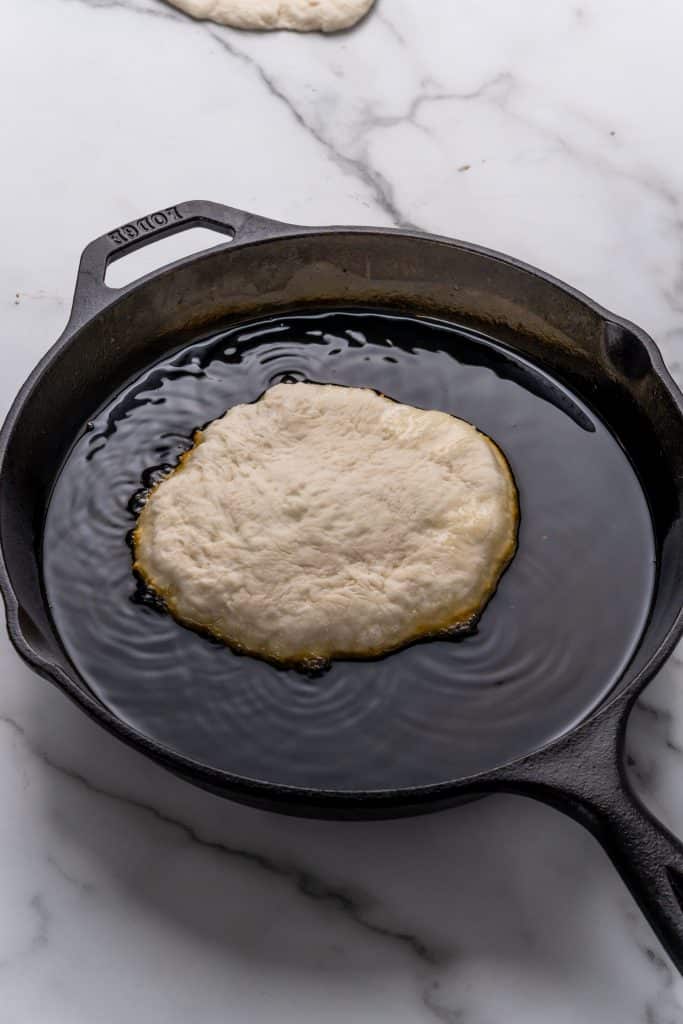a piece of Indian fry bread in a cast iron skillet filled with hot oil