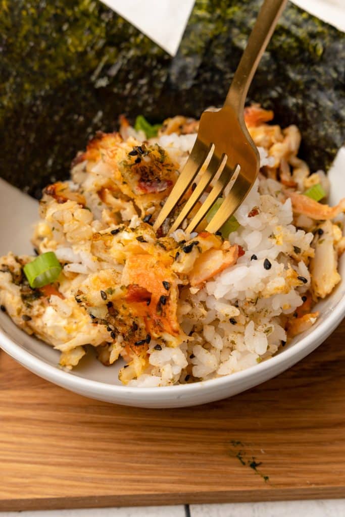 a gold fork digging into a white bowl filled with sushi bake