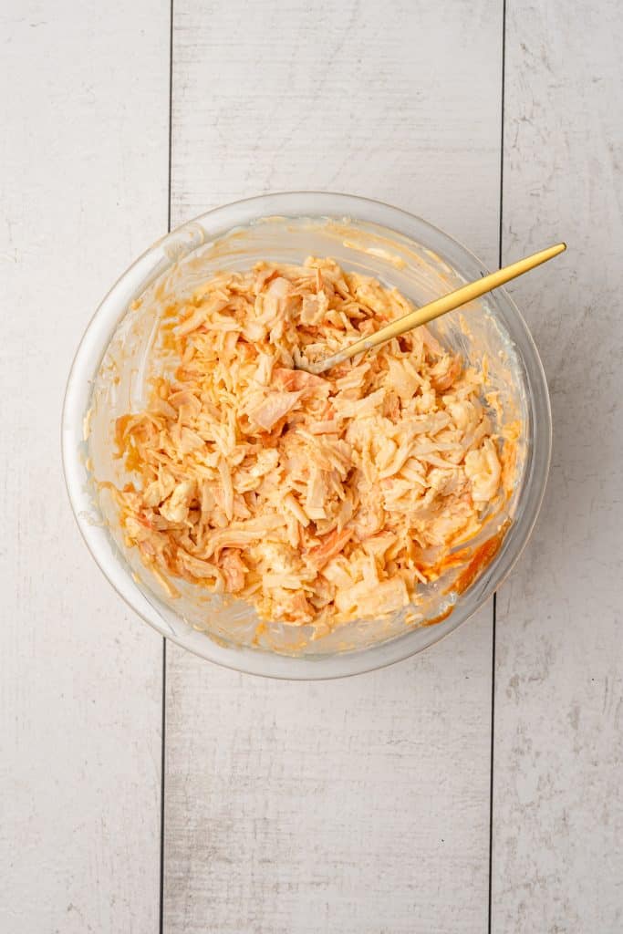 creamy crab mixture in a glass mixing bowl with a wooden spoon