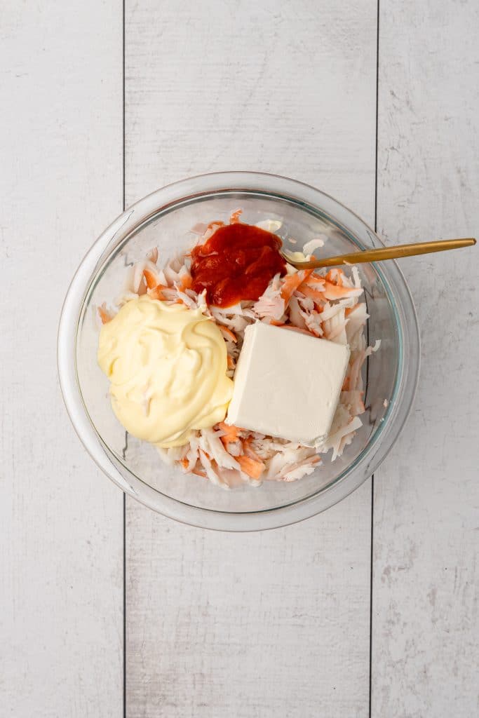imitation crab and creamy ingredients in a glass mixing bowl with a wooden spoon