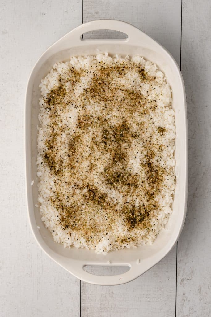 sushi rice and seasonings spread in a white casserole dish