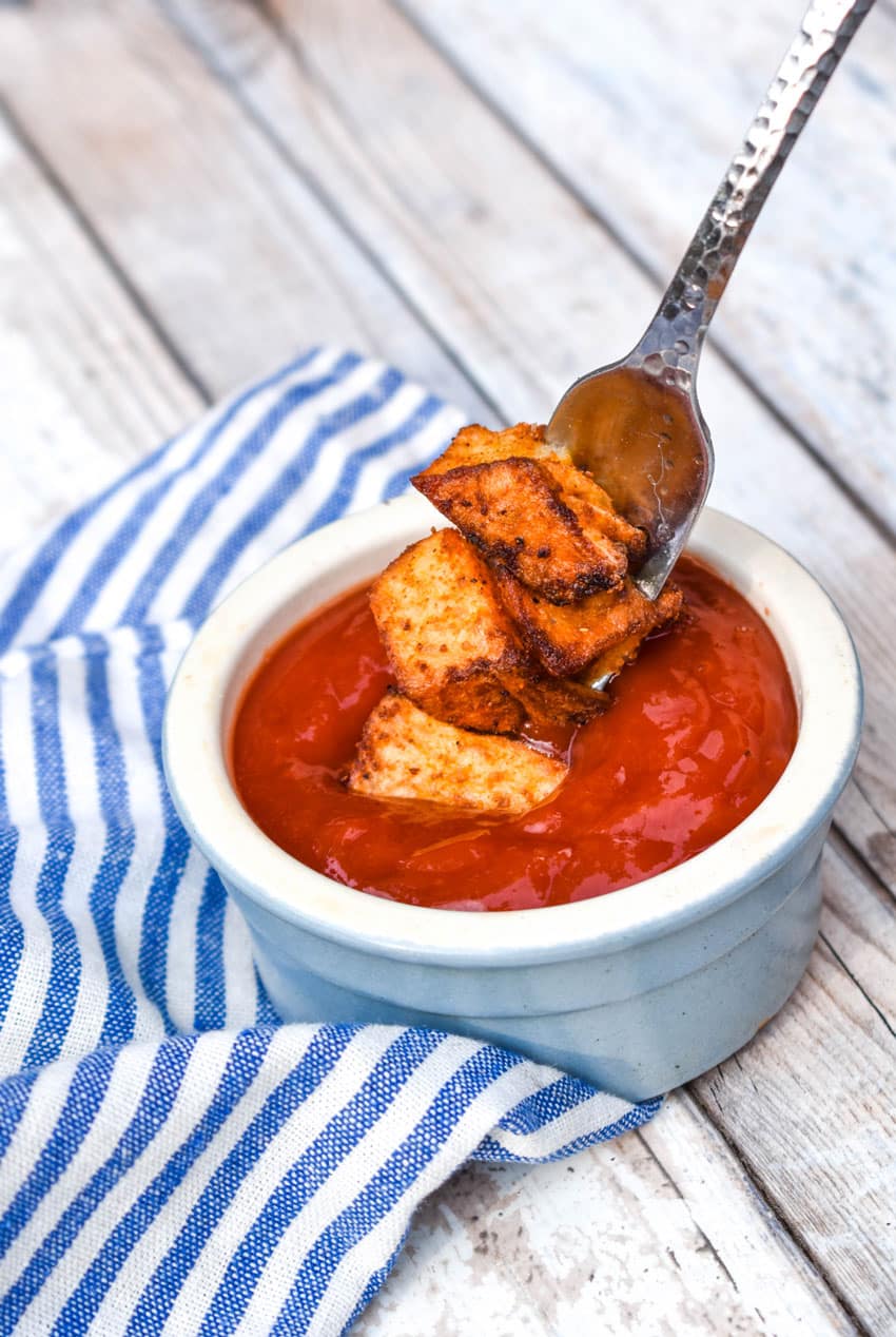 crispy home fries on a silver fork being dipped into a small bowl of ketchup