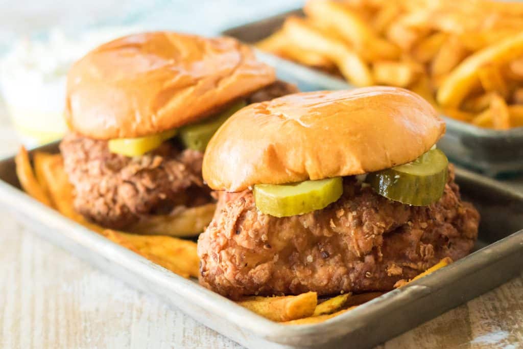 two copycat popeyes chicken sandwiches on a metal tray with french fries