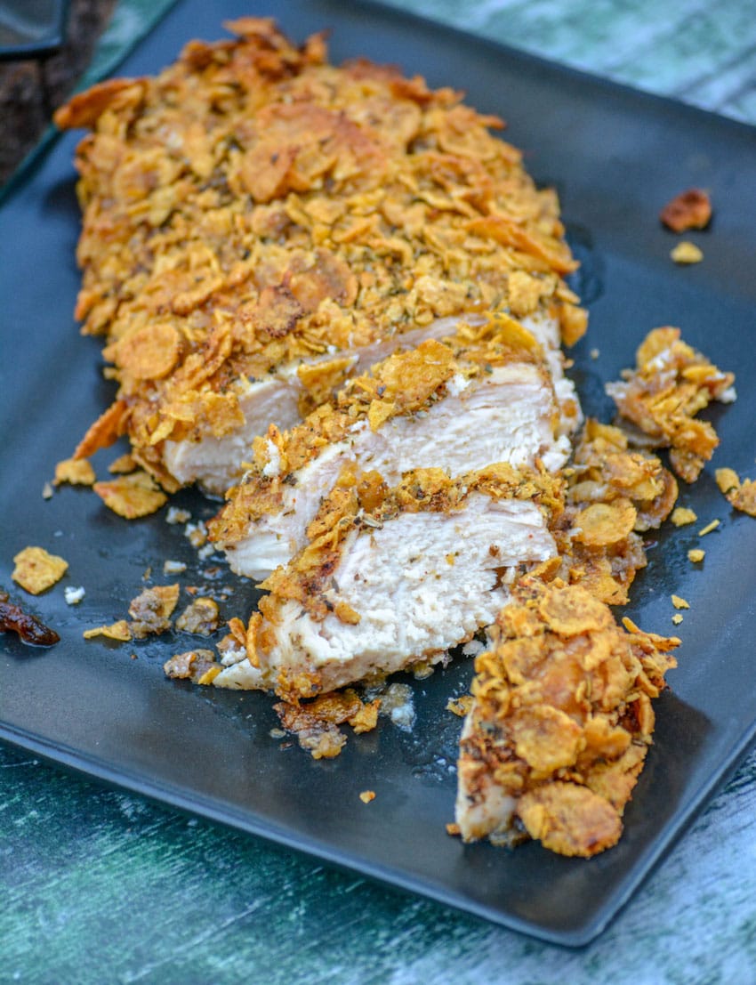 a sliced piece of baked crispy cornflake chicken on a black plate