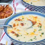 a silver spoon in a bowl of quick and easy potato soup topped with bacon, cheese, and chives