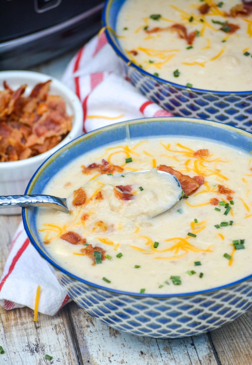 a silver spoon in a bowl of quick and easy potato soup topped with bacon, cheese, and chives