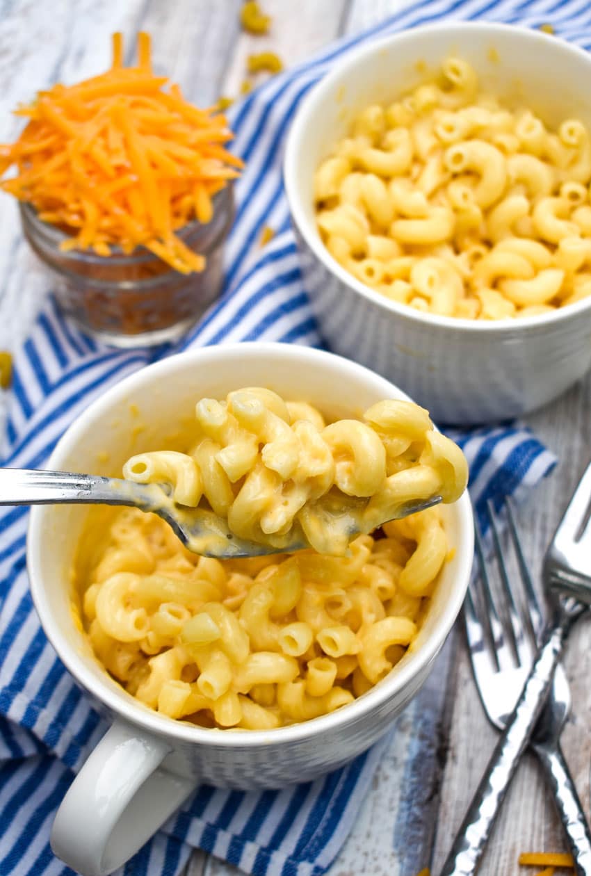 a silver fork lifting a scoop of creamy microwave mac and cheese out of a white mug